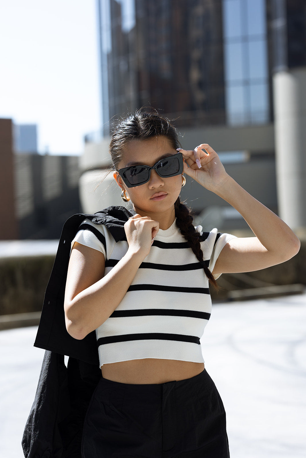 Person wearing a black and white striped shirt with sunglasses and a black jacket over shoulders.