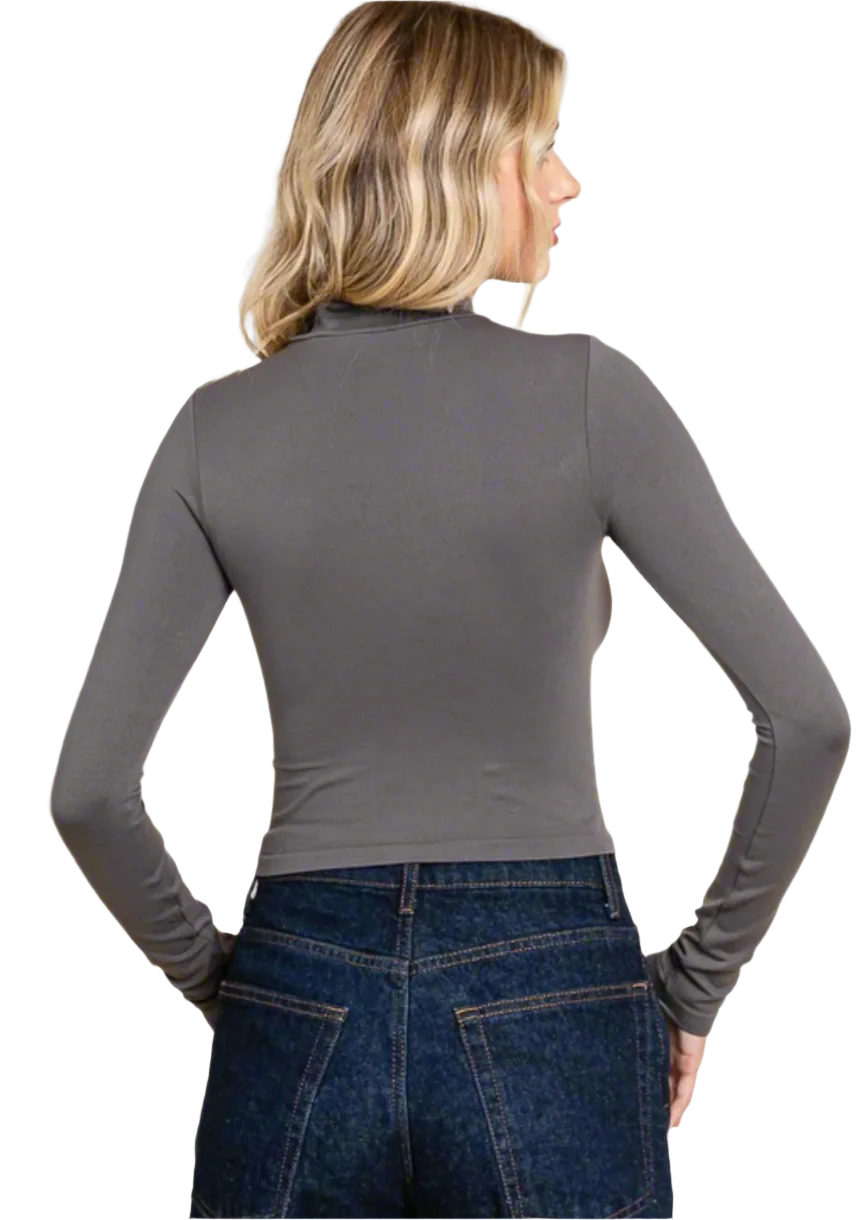 Woman wearing a gray long-sleeve top and blue jeans against a plain background