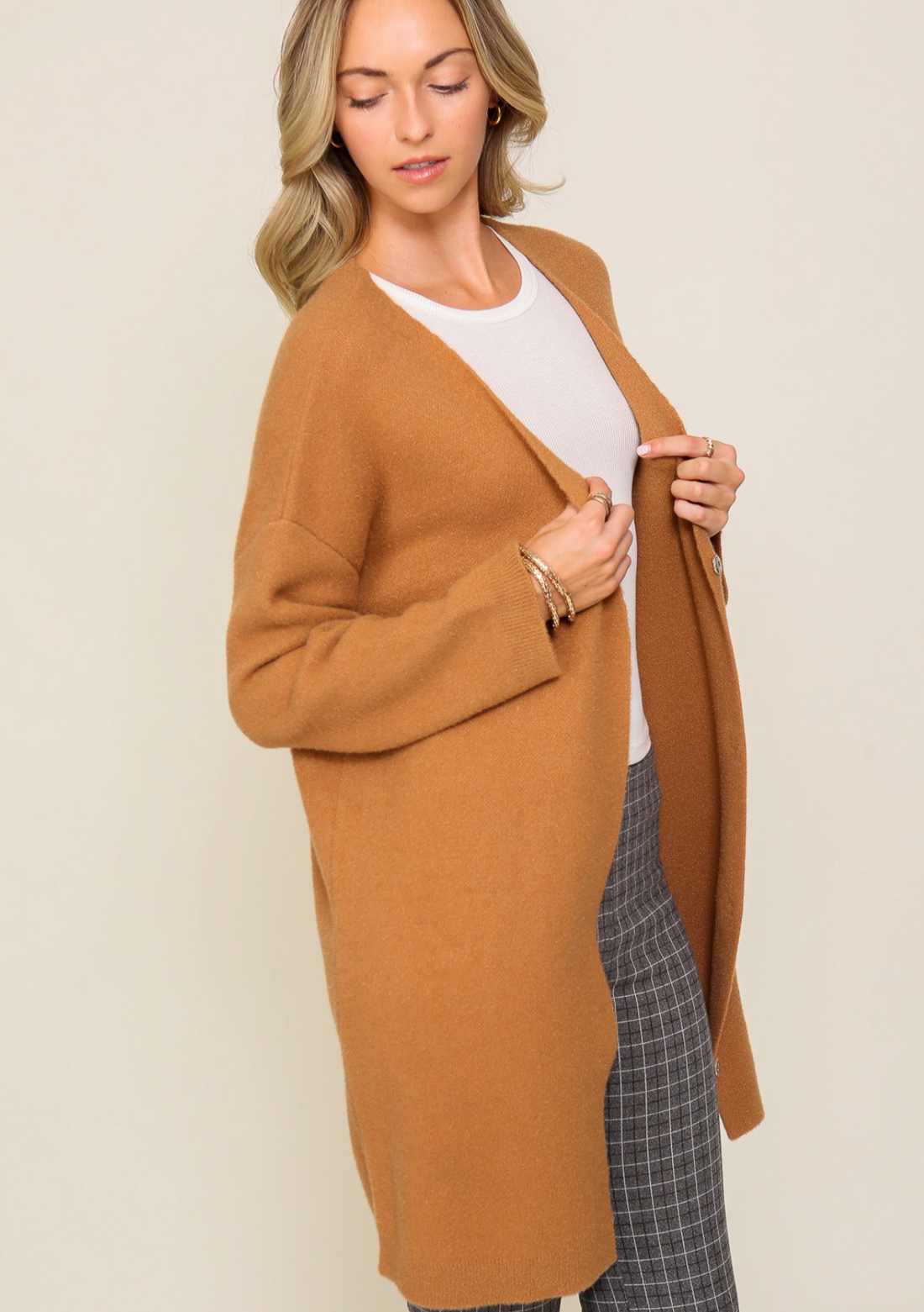 A woman wearing a brown oversized button-down cardigan with long sleeves, paired with a white top and checkered pants.