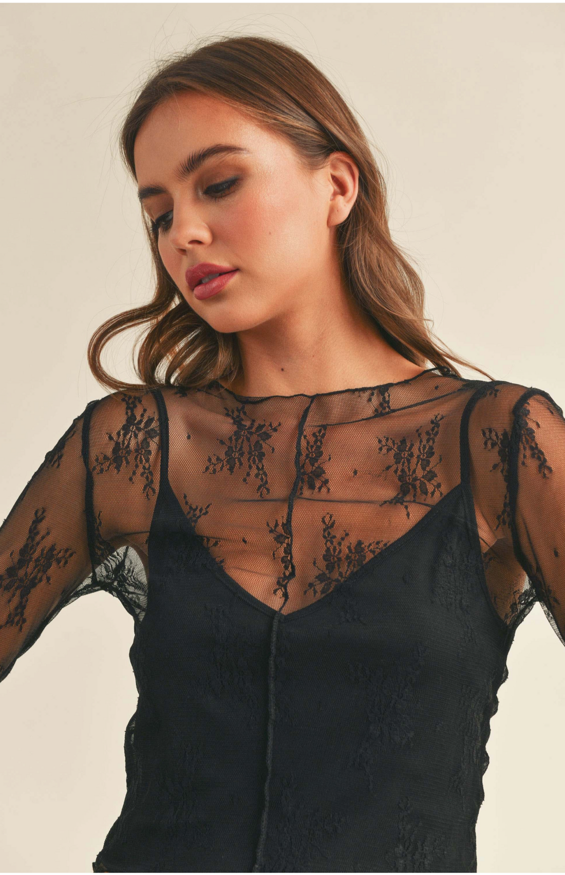 A female model wearing a black lace long-sleeve top with fabric lining insert.