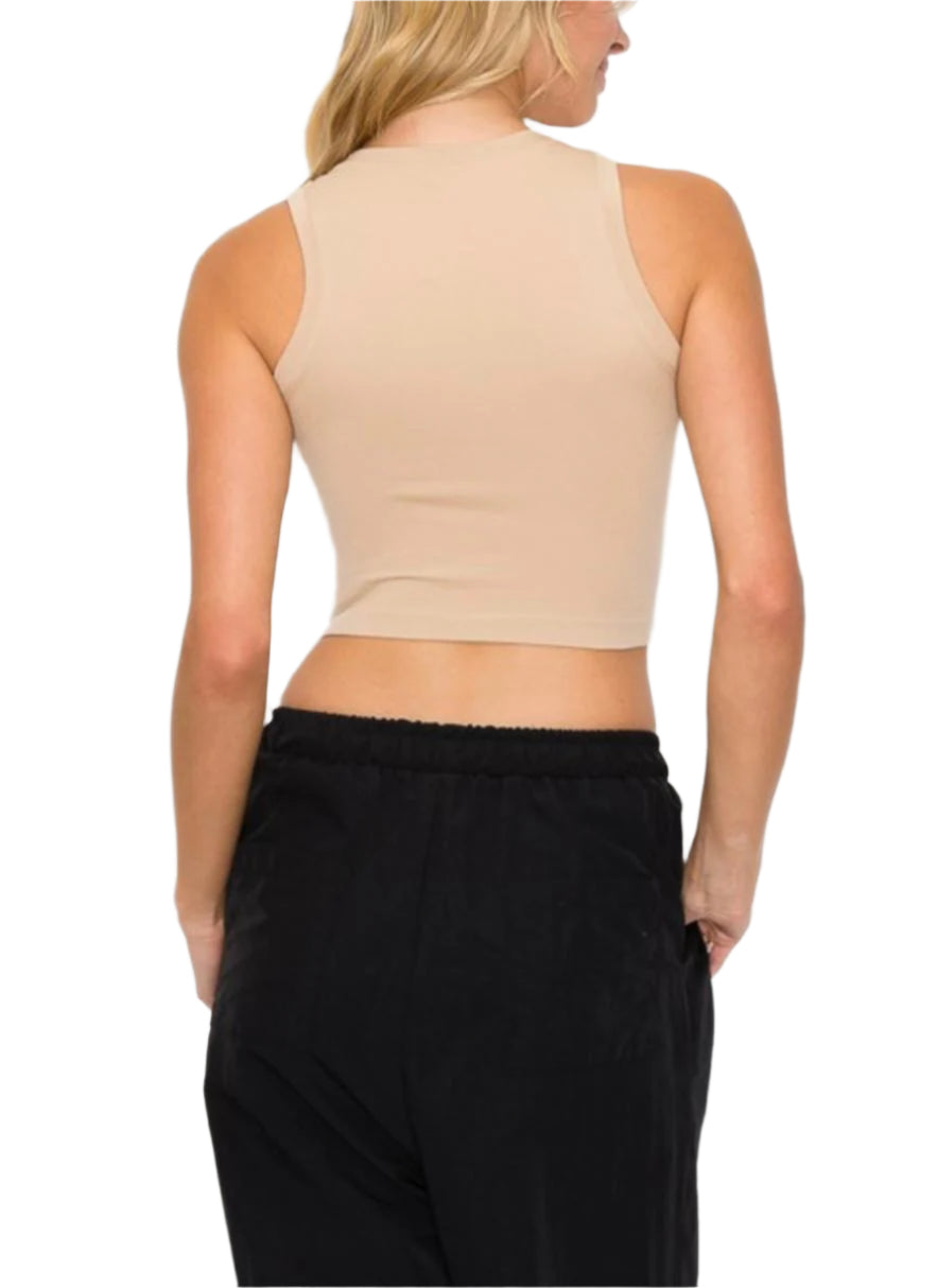 A female model wearing a round neck sleeveless top in beige, paired with black trousers.