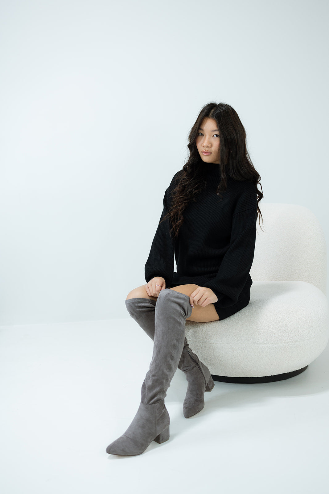Person wearing a black outfit and gray knee-high boots on a white background