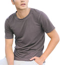 Man wearing a gray t-shirt sitting outdoors with greenery in the background