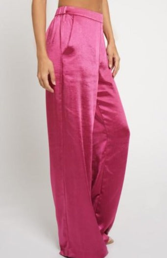 A model wearing pink satin trousers with an elastic waistband and side pockets, standing against a white background.