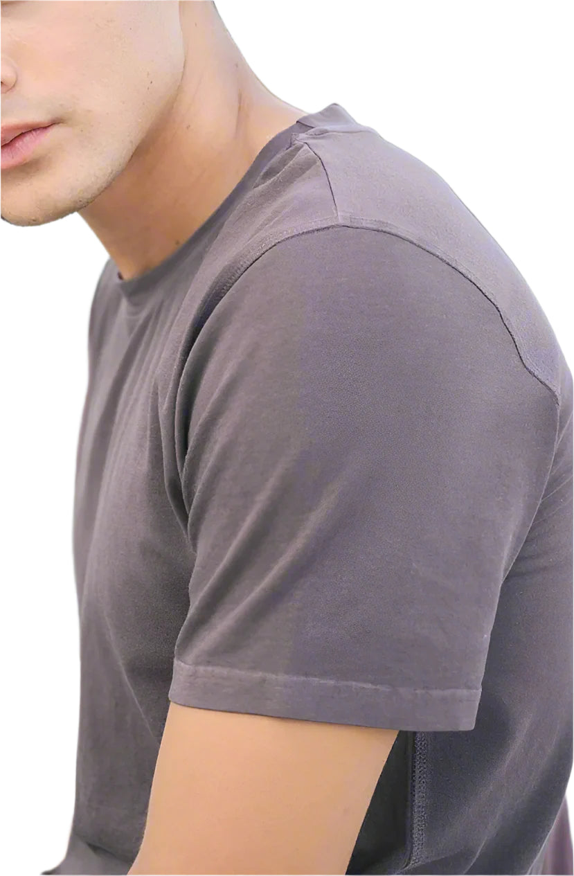 Man wearing a gray t-shirt sitting outdoors with greenery in the background