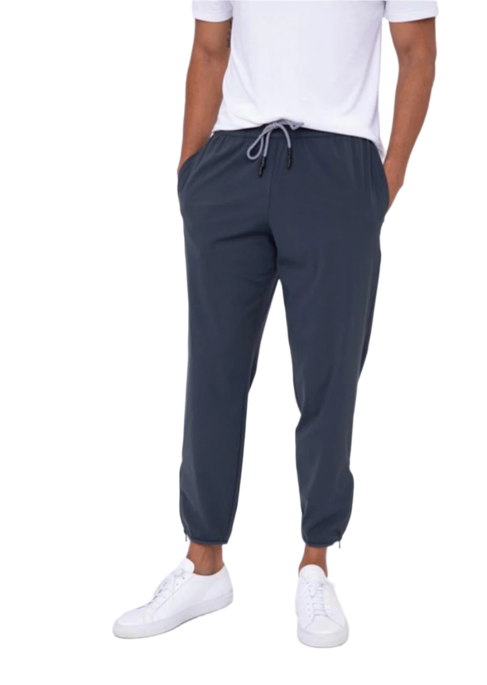 A person standing wearing high-waisted gray joggers and white sneakers.