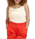 Woman wearing a beige top and red pants against a gray background.