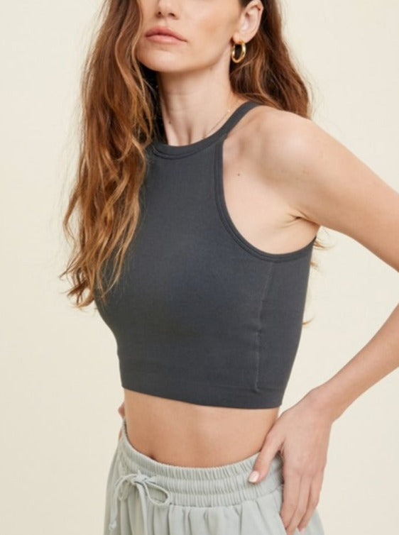 A woman wearing a seamless ribbed high neck top in gray, with a necklace and a white jacket over it.