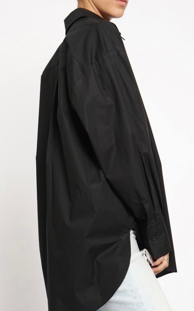 A woman wearing an oversized black button down shirt with a collar and long sleeves, paired with a white cropped top and blue ripped jeans.