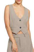A female model wearing a beige woven vest with a deep V-neckline, two-button closure, and a pocket detail.
