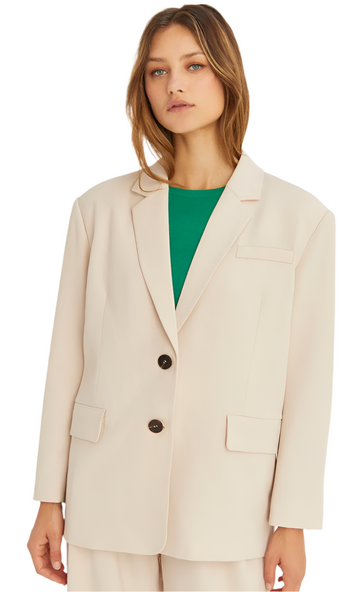 A woman wearing a beige single-breasted blazer with a notched collar and a front flap pocket, paired with a green top and trousers.