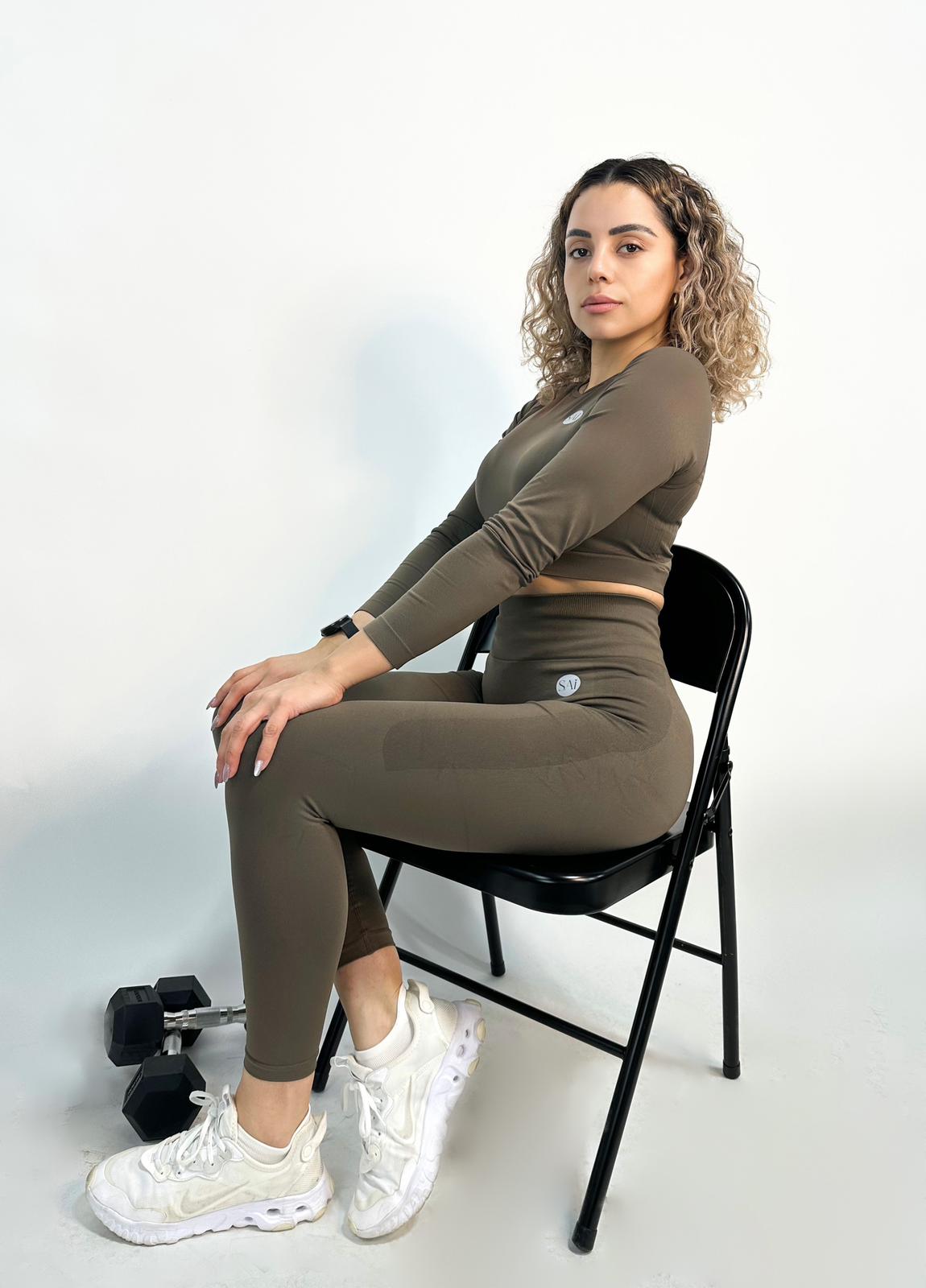 Woman sitting on a chair wearing a brown athletic outfit with white sneakers.