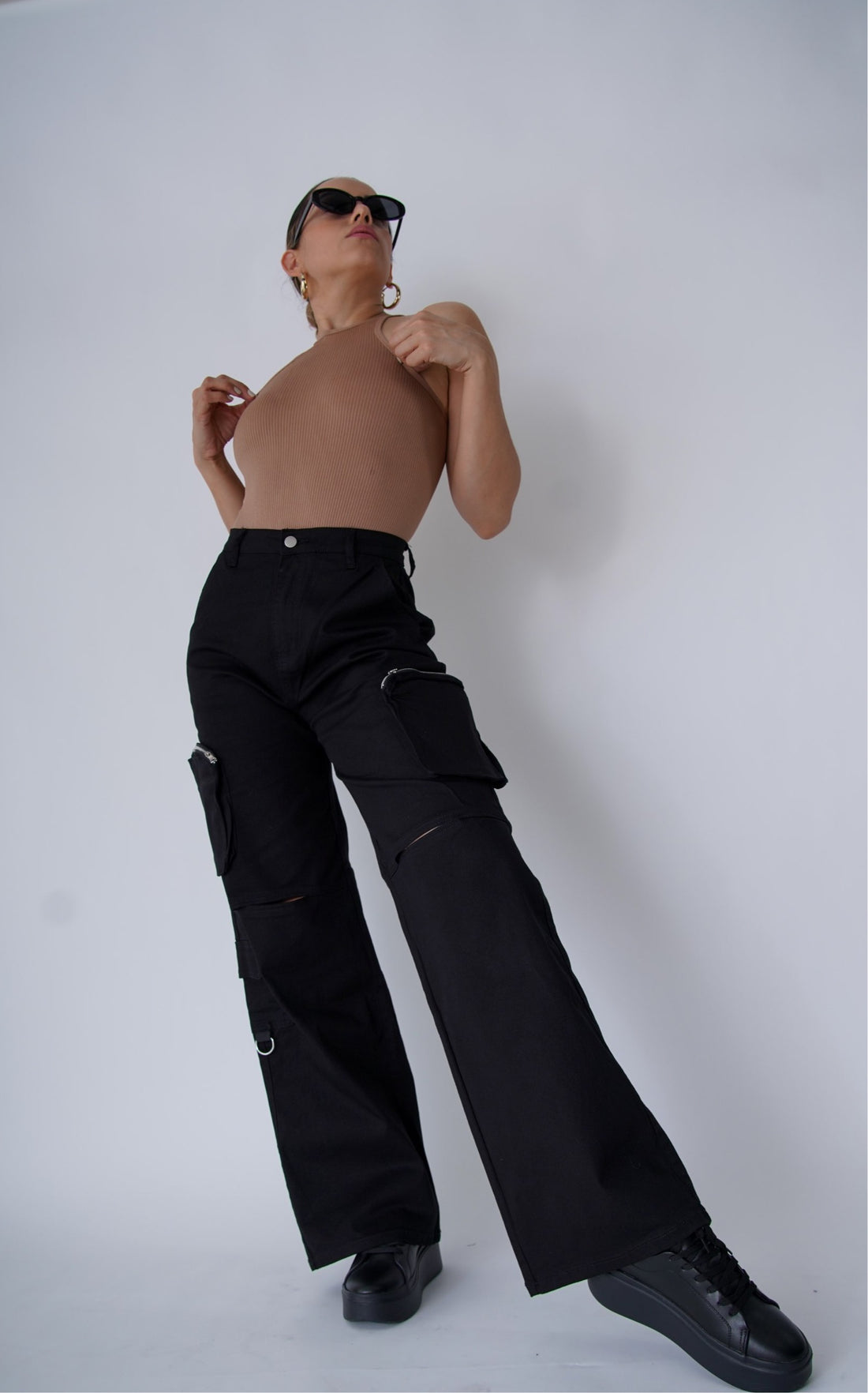 Woman wearing a beige ribbed top and sunglasses against a plain background