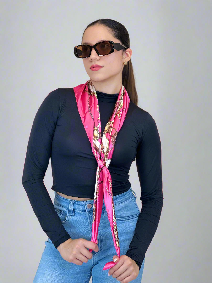 Woman wearing a pink scarf with gold accents, dark long-sleeve top, and blue jeans against a beige background.
