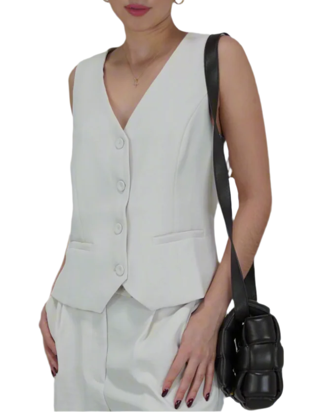 Woman wearing a white vest and holding a black bag against a plain background