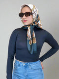 Woman wearing a patterned headscarf, sunglasses, navy top, and blue jeans on a beige background