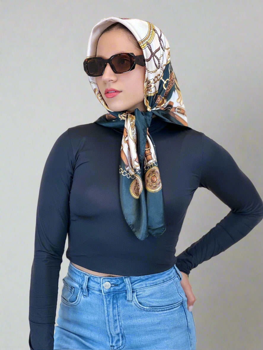 Woman wearing a patterned headscarf, sunglasses, navy top, and blue jeans on a beige background