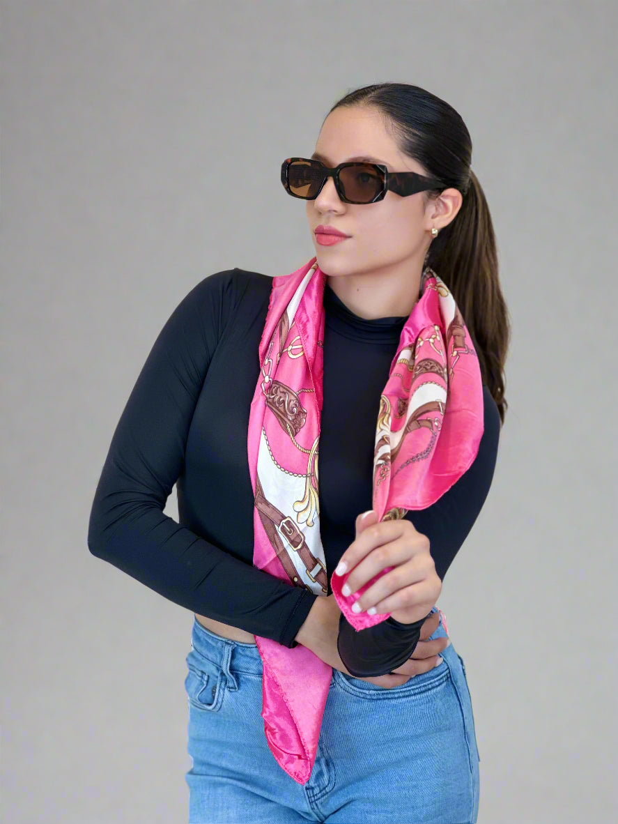 Woman wearing a pink scarf with a pattern, black sunglasses, and blue jeans against a beige background