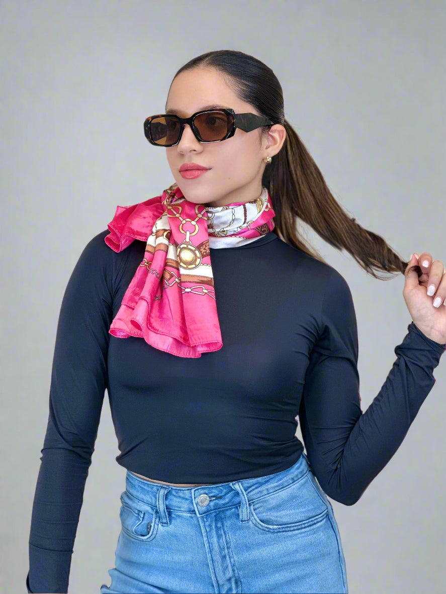 Woman wearing a navy long-sleeve top, blue jeans, and a pink scarf with sunglasses on a beige background