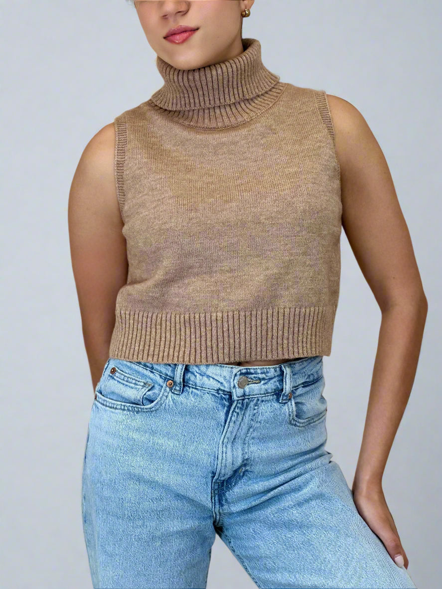 Person wearing a brown sleeveless turtleneck sweater and blue jeans on a beige background