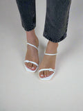 White open-toe sandals worn with black jeans on a beige background