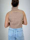 Person wearing a beige sleeveless knitted top and light blue jeans on a beige background