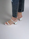 White sandals worn with black jeans on a beige background