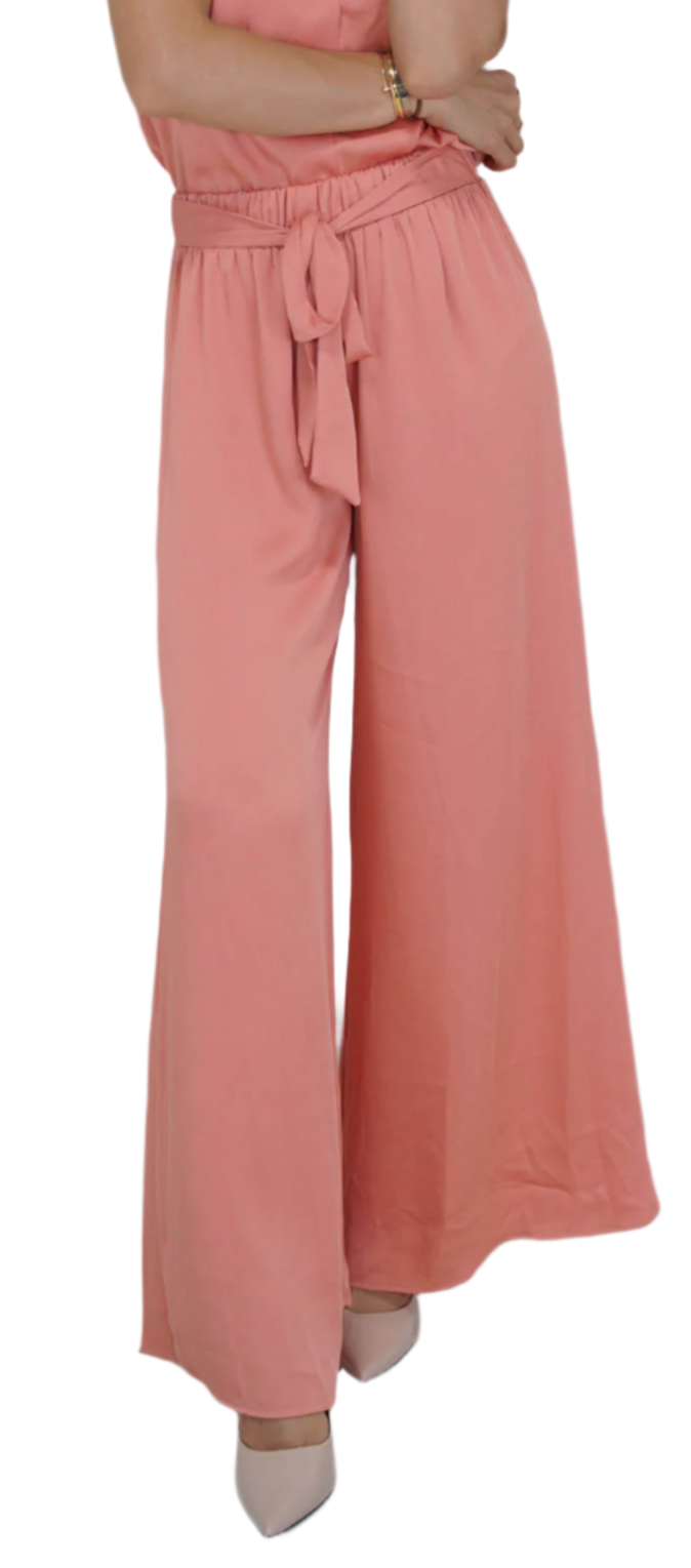A woman standing, wearing apricot silk wide leg pants with a tie waist and a chic belt.