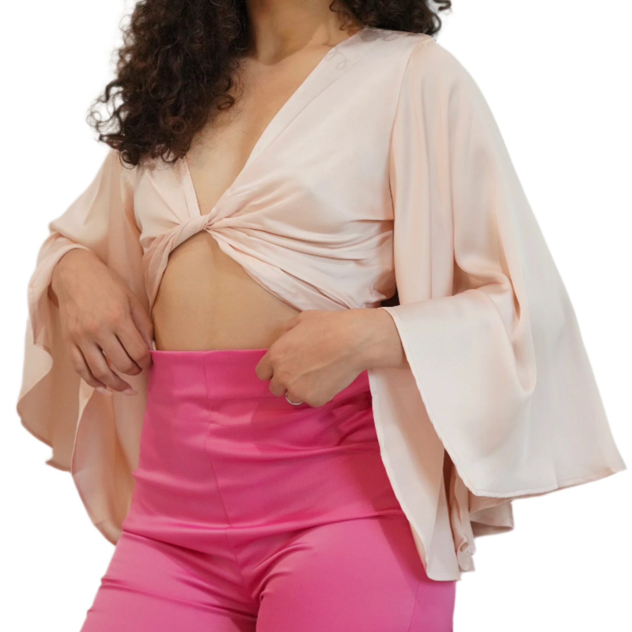 Woman wearing a light pink top with bell sleeves and bright pink pants on a white background