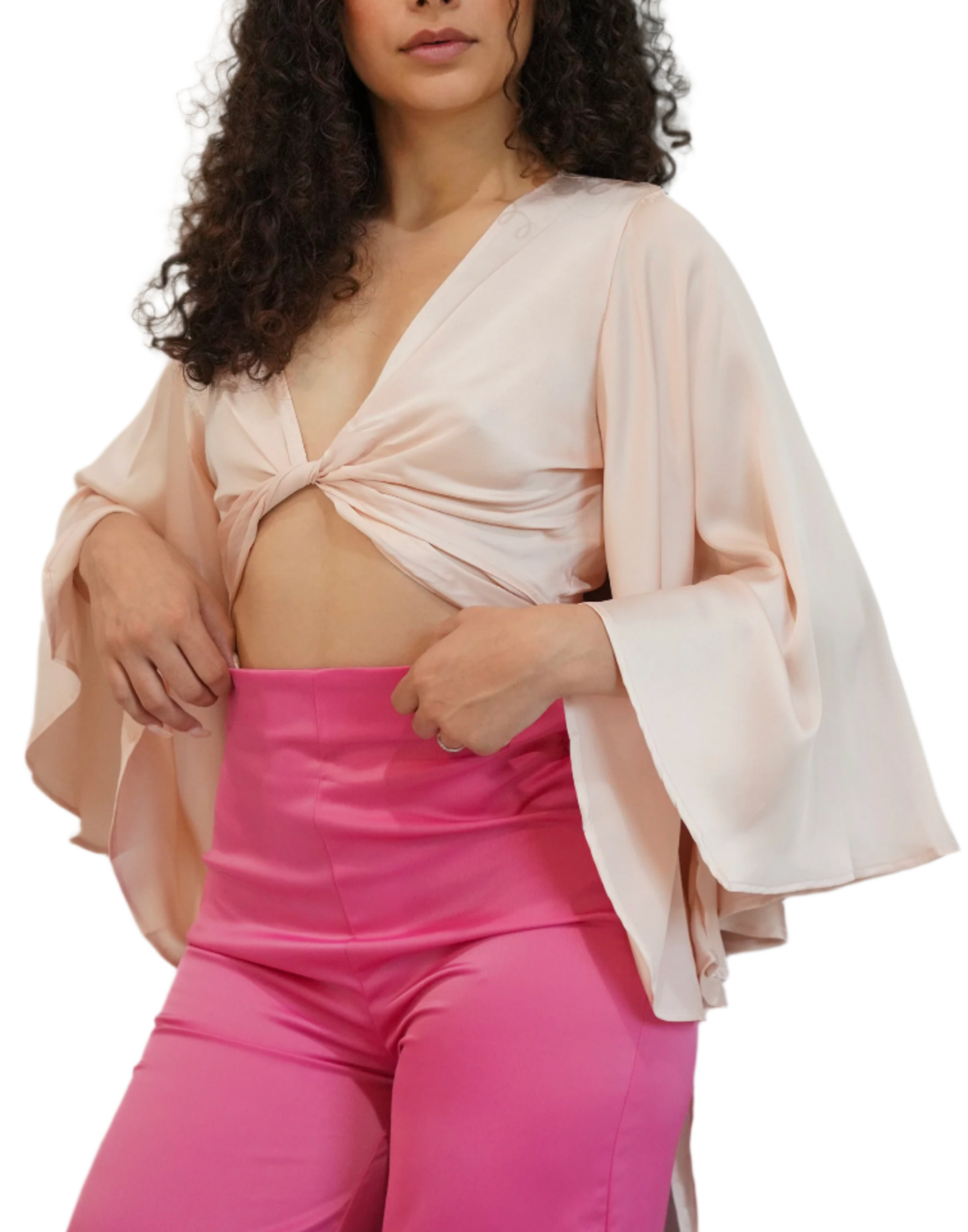 Woman wearing a light pink top with bell sleeves and bright pink pants on a white background