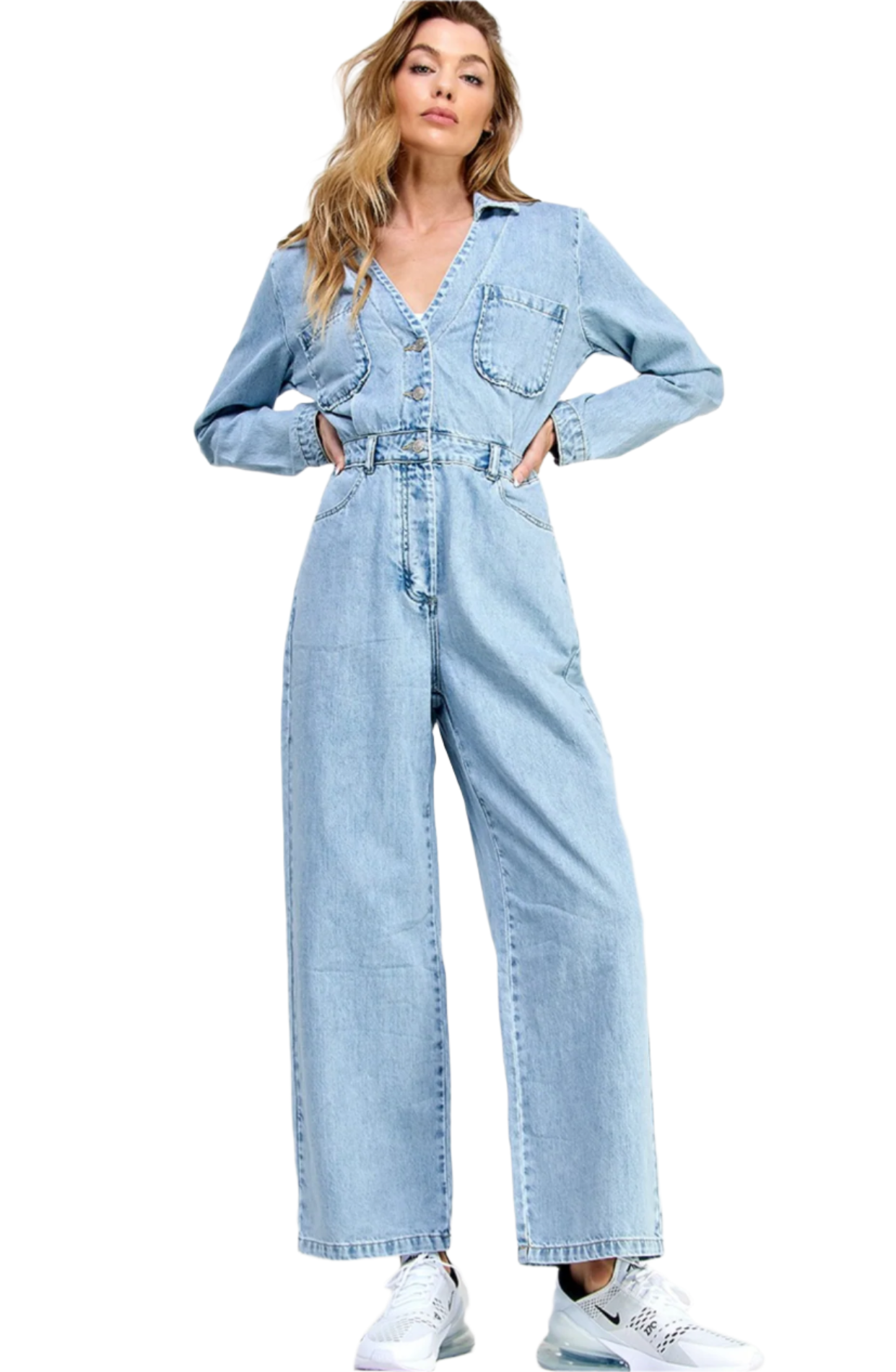 A female model wearing a blue denim jumpsuit with a collar, long sleeves, and straight pants, paired with white sneakers.