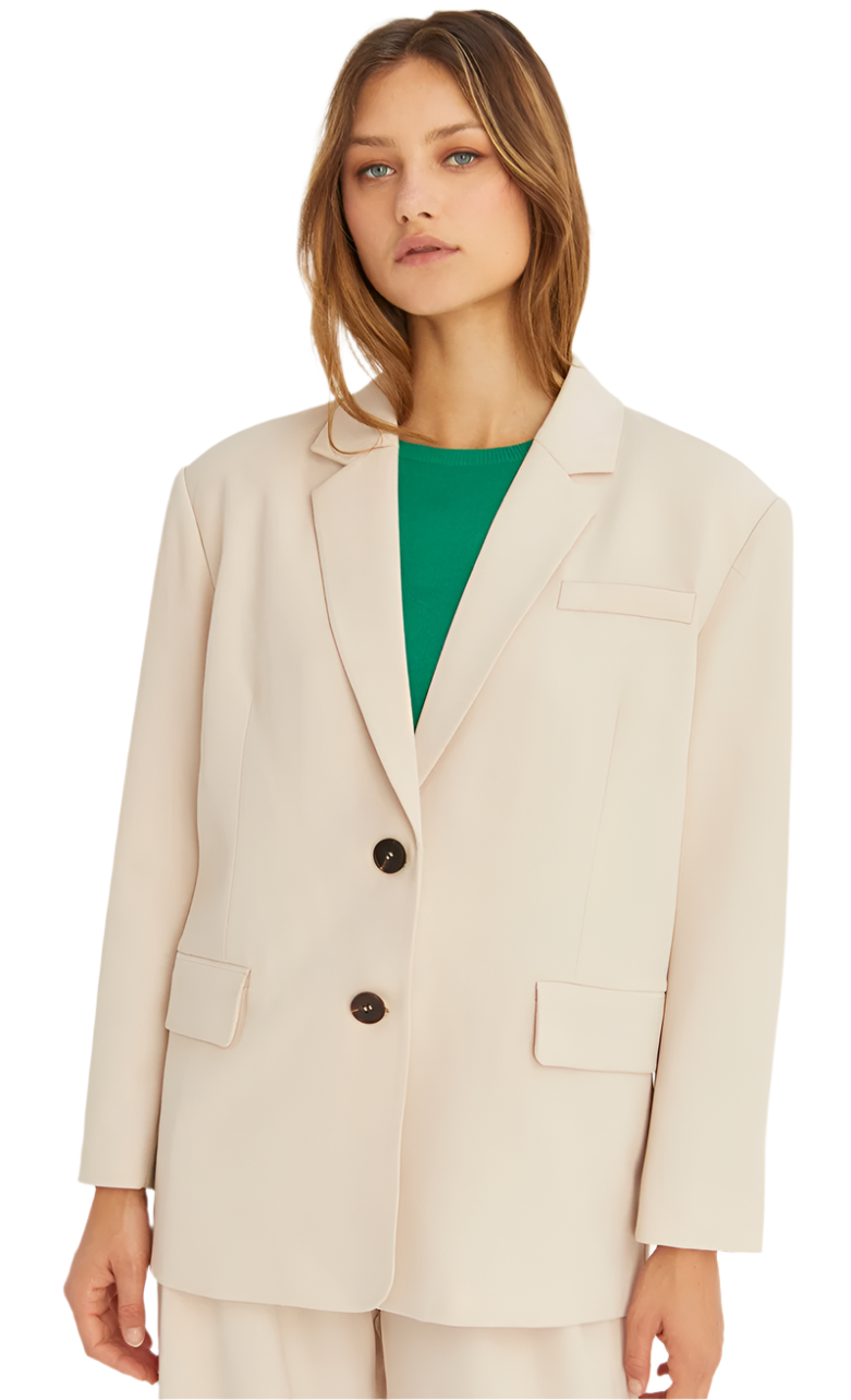 A woman wearing a beige single-breasted blazer with a notched collar and a front flap pocket, paired with a green top and trousers.