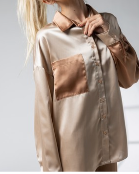 A female model wearing a beige, button-up, satin blouse with a collared neckline.