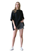 Woman wearing a black oversized T-shirt and denim shorts standing in a room with a white backdrop